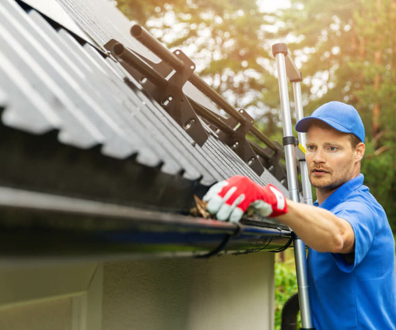 worker cleaning debris out of roof gutter