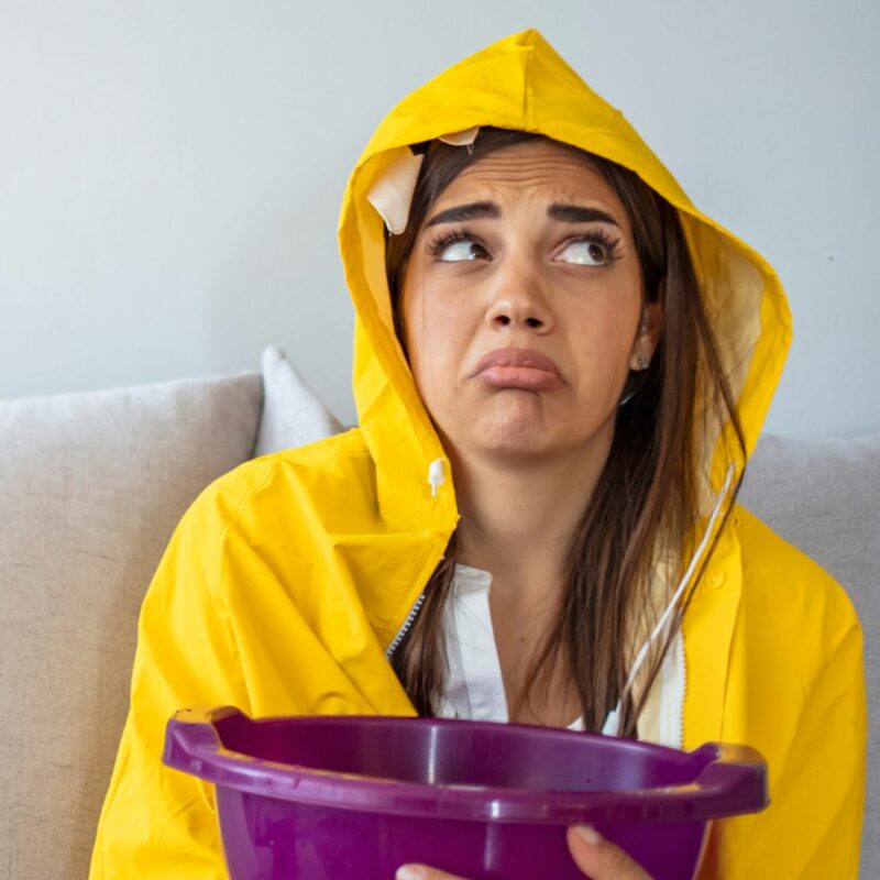 girl sitting on couch with bucket under ceiling leak